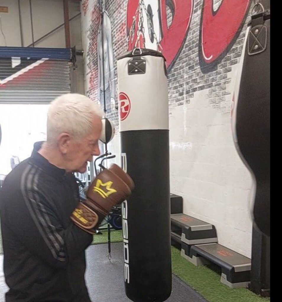 Frank Gilfeather demonstrating boxing techniques in a gym, surrounded by custom-designed boxing gloves from his collection