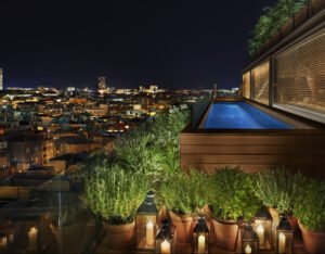 The rooftop terrace of The Rome EDITION Hotel with a serene pool, lounge seating, and panoramic views of Rome’s skyline