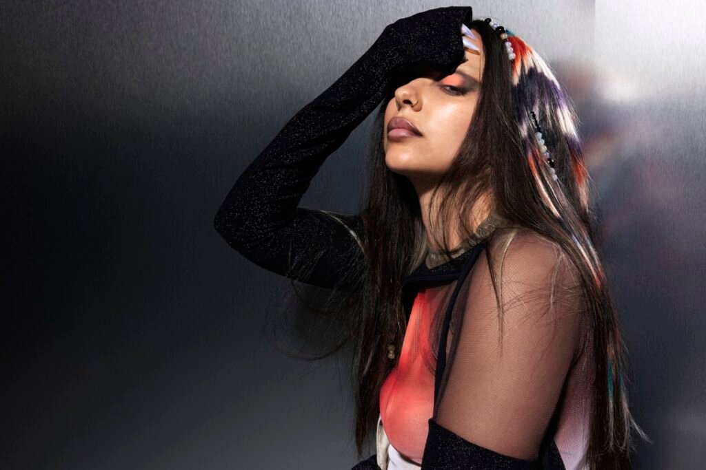 JADE performing her hit single “IT Girl” with a confident pose, vibrant outfit, and shattered crockery in the background