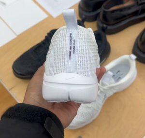 A close-up of the CdG x Nike Air Rejuven8 sneaker, featuring a minimalist black and white design with modern materials