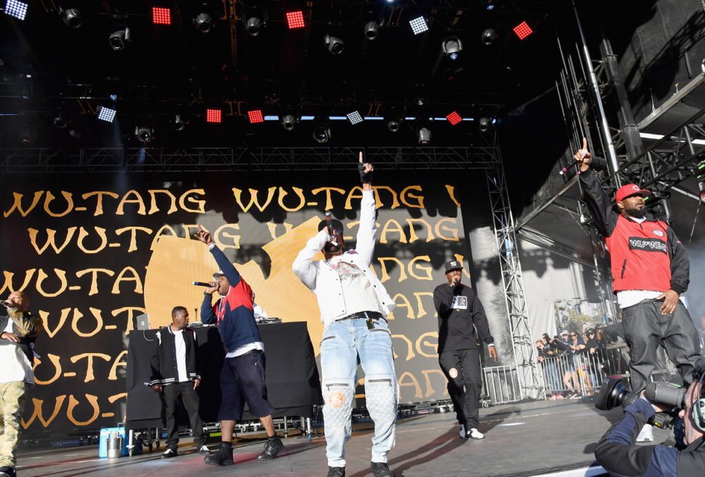 Wu-Tang Clan performing on stage with the iconic “W” logo glowing behind them