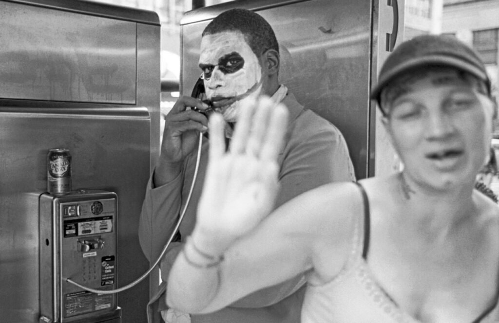 A photograph by Daniel Weiss from Pay Phone showing a weathered NYC pay phone booth with a passerby in soft focus