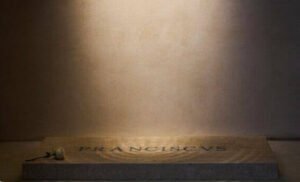 Close-up of Pope Francis’ mock tombstone inscription showing unevenly spaced Latin lettering carved into white marble