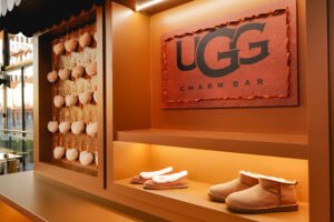 UGG retail display featuring a “UGG Charm Bar” sign, with shelves showcasing classic shearling-lined boots and slippers, alongside a wall of fluffy keychain charms.