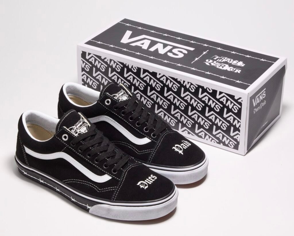 Travis Barker x Vans Old Skool “Dues Paid” sneakers displayed beside their co-branded box, featuring black uppers with white side stripes, gothic “Dues” and “Paid” embroidery on the toe boxes, barbed-wire print around the midsoles, and matching monochrome packaging with Vans and Travis Barker logos