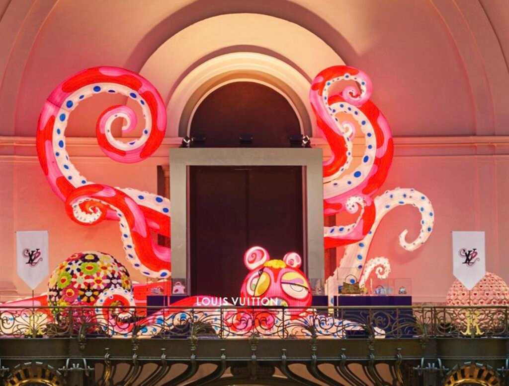 Installation view of Louis Vuitton’s Artycapucines VII presentation at Art Basel Paris 2025, featuring Takashi Murakami’s large pink-and-red polka-dotted tentacle sculptures and colorful flower spheres surrounding the Louis Vuitton display inside the Grand Palais.