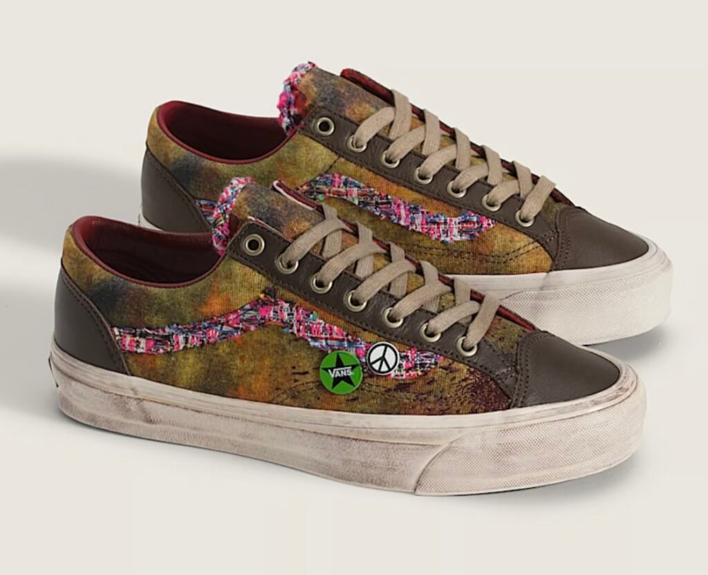 Vans Premium Old Skool “Souvenir” in Warm Brown — a pair of low-top sneakers featuring a distressed brown canvas base with glossy leather overlays, multicolored tweed side stripes, tan laces, and vintage-style souvenir pins including a green Vans star and peace symbol on the lateral side, all set on an aged off-white vulcanized sole.