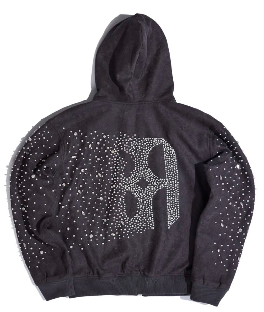 Back view of a charcoal-grey hoodie embellished with pearl and crystal studs forming a large ornate “B” design at the center. The scattered rhinestones across the sleeves and shoulders create a shimmering, galaxy-like effect against the soft suede-textured fabric.