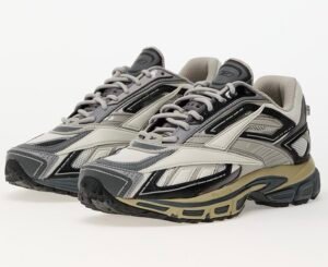 Pair of Reebok Premier Road Ultra Tonal Grey sneakers featuring layered mesh and leather panels in shades of grey, black, and beige, with a sculpted DMX Ride midsole and Reebok Vector logo on the side, photographed on a white background.