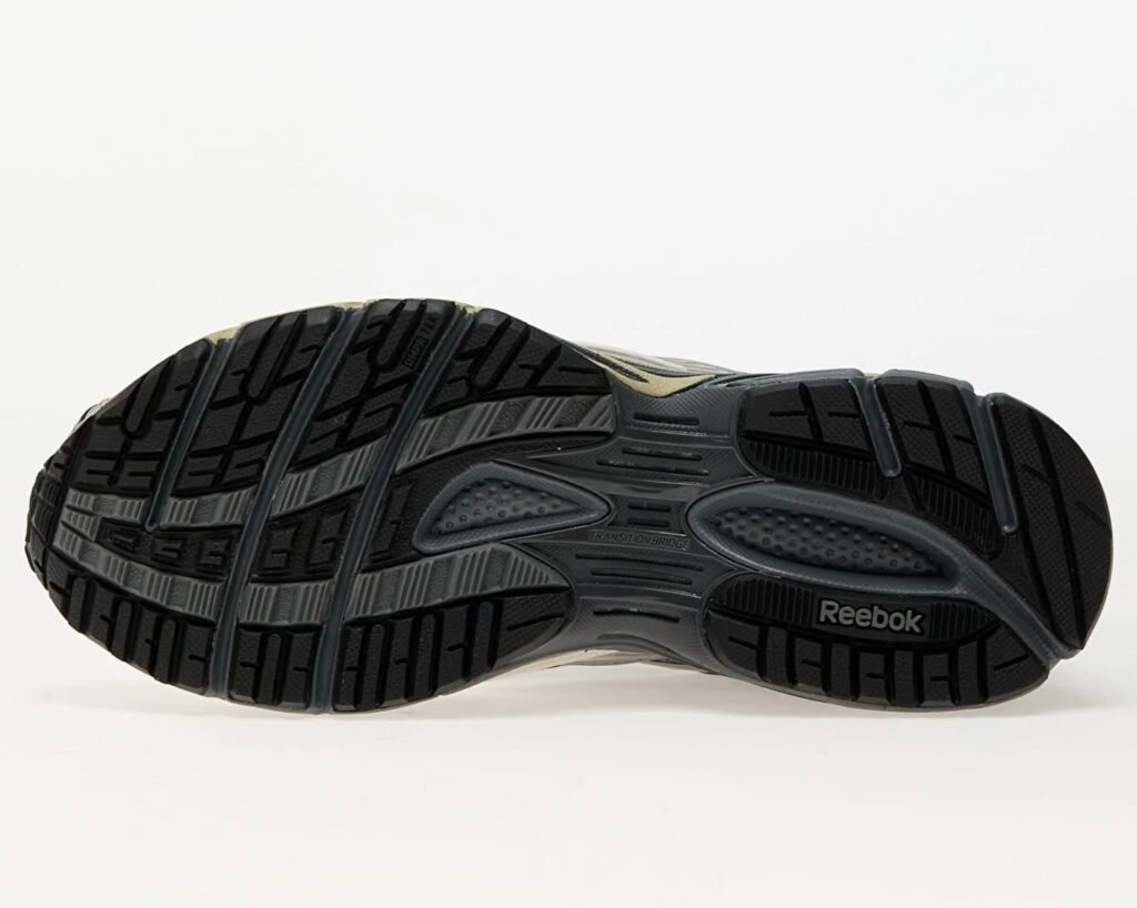 Bottom view of the Reebok Premier Road Ultra Tonal Grey sneaker, showcasing the black rubber outsole with detailed tread pattern, “Transition Bridge” midfoot support, and Reebok logo embossed near the heel for traction and stability design.