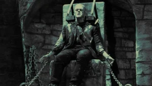 Classic black-and-white depiction of Frankenstein’s Monster strapped to a stone chair with chains, wearing torn clothes, from early Universal horror cinema.