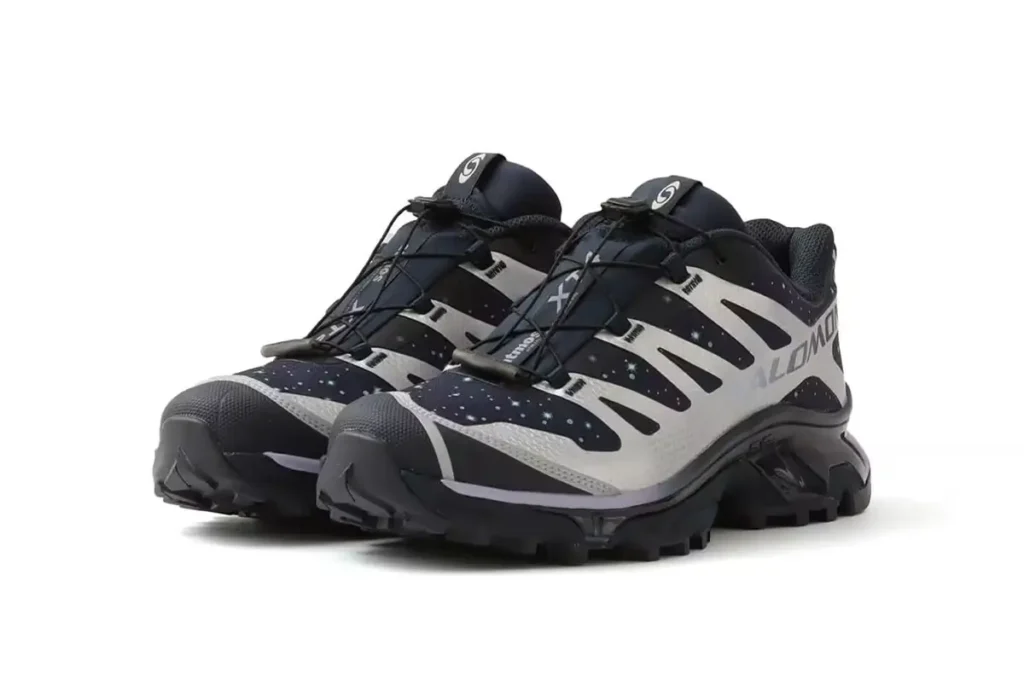 A pair of atmos × Salomon XT-4 OG GTX “Stars Collide” sneakers featuring a navy-to-black cosmic gradient upper with star-speckled detailing, silver TPU support overlays, black speed-lace system, and rugged trail-ready Contagrip outsole