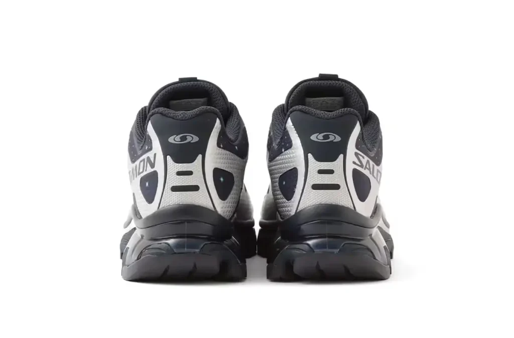 Rear view of the atmos × Salomon XT-4 OG GTX “Stars Collide” showing the dual heel panels, silver and navy cosmic-speckled overlays, Salomon branding, and the sculpted black trail midsole and outsole