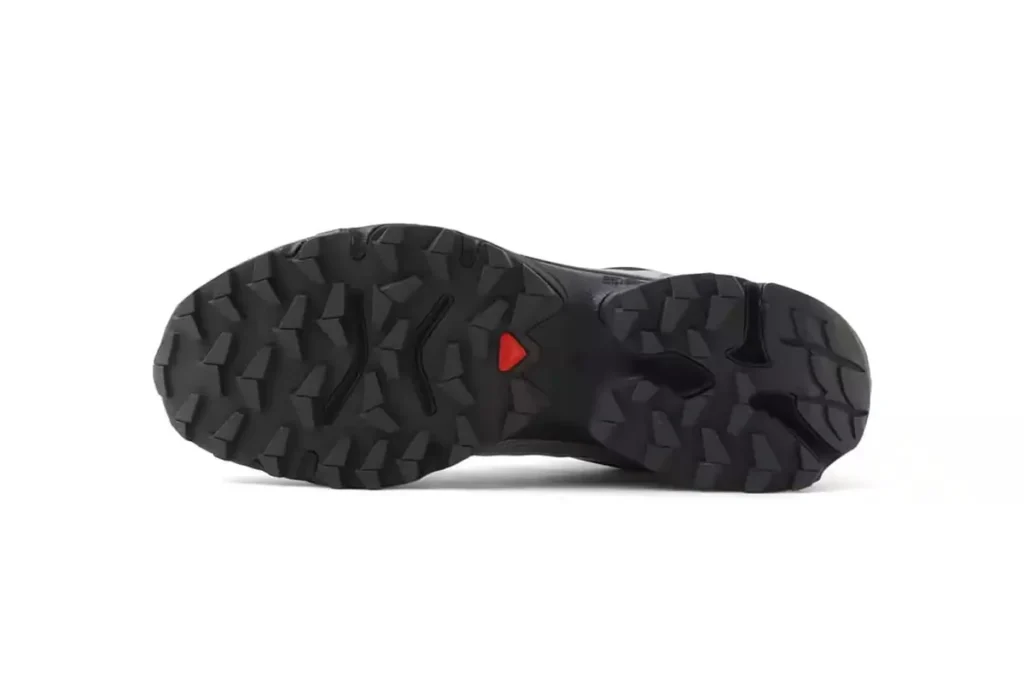 Bottom view of the atmos × Salomon XT-4 OG GTX “Stars Collide” showing the rugged black Contagrip outsole with deep multi-directional lugs and a small red traction marker at the midfoot
