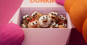 Animated Dunkin’ Munchkins inside a pink Dunkin’ box, each donut hole decorated with expressive eyes and smiling mouths, creating a lively, character-filled scene as gloved hands hold the box against a bright pink background