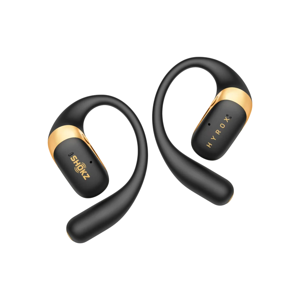 Pair of Shokz × HYROX limited-edition wireless open-ear sport headphones in matte black with metallic gold accents, displayed on a black background emphasizing their ergonomic loop design and premium athletic collaboration styling.