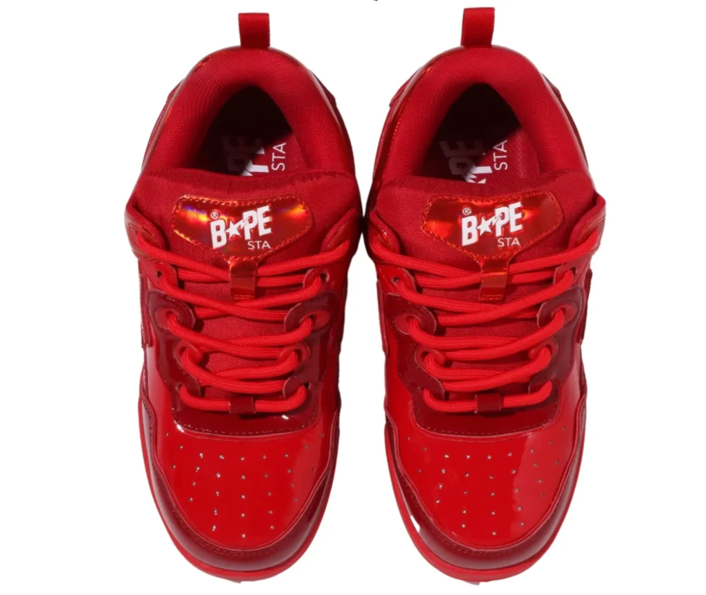 A close-up top-down view of the Bape US Limited Flip Sta Red sneaker, focusing on the padded red tongue with the woven A Bathing Ape label, red flat laces, and smooth white leather vamp. The contrast between the bright red overlays and crisp white panels is accentuated by the clean studio lighting, showcasing the sneaker’s construction and premium finish