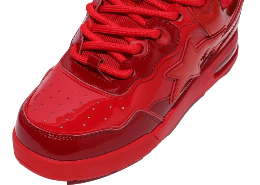 A close-up angled side view of the Bape US Limited Flip Sta Red sneaker, emphasizing the raised red BAPE heel badge, glossy red heel overlay, and the clean transition into the white leather quarter panel. The flipped star logo is partially visible toward the midfoot, while studio lighting highlights the texture, stitching, and bold red-and-white contrast