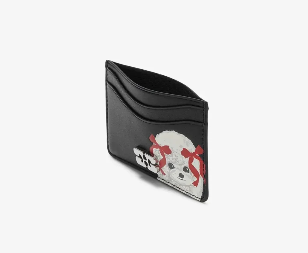 Angled view of the Ganni Bou Card Holder in black recycled leather showing the front poodle illustration with red ribbons and silver logo hardware, highlighting the dual card slots and open top compartment against a white background