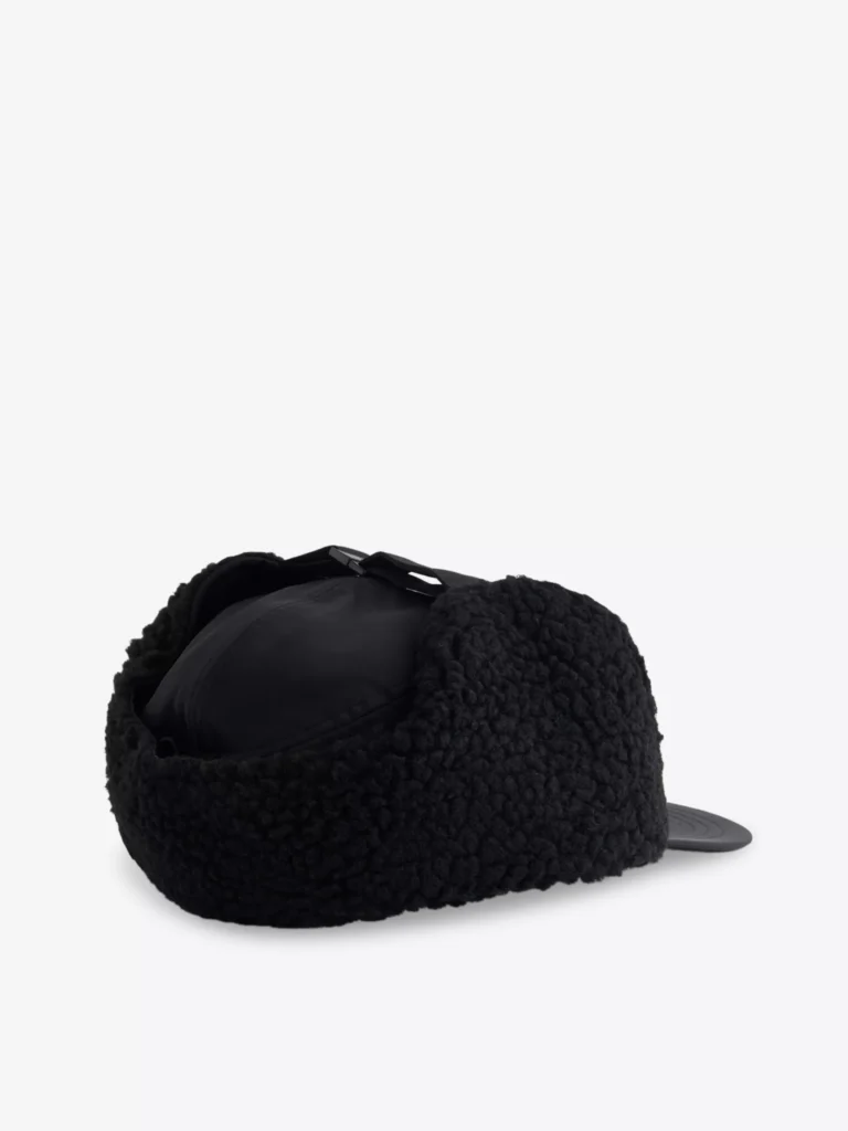 Side view of the Carhartt WIP Oltera Ear-Flap Woven Cap in black, showing the soft fleece ear flaps folded up around the crown for a snug, winter-ready silhouette