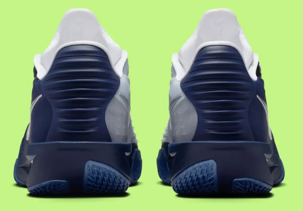 Rear view of the Nike GT Cut 3 Turbo Mavericks edition, showing the sculpted navy heel counters, white padded collars, gradient side panels, and blue traction outsoles, set against a bright lime-green background