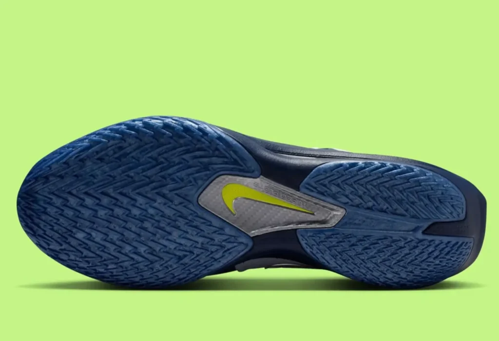 Bottom view of the Nike GT Cut 3 Turbo Mavericks edition, showing the blue herringbone traction outsole with a central carbon-fiber shank and neon-yellow Swoosh, set against a bright lime-green background