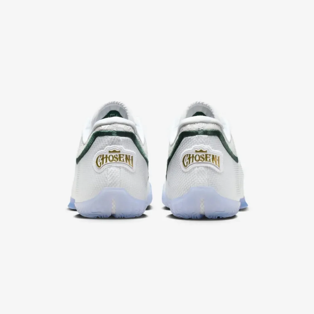 Rear view of the Nike LeBron 23 “From This Point Forward,” showing the white heel panels with green trim and a gold-outlined “CHOSEN 1” emblem on each shoe, set above translucent icy outsoles on a clean white background
