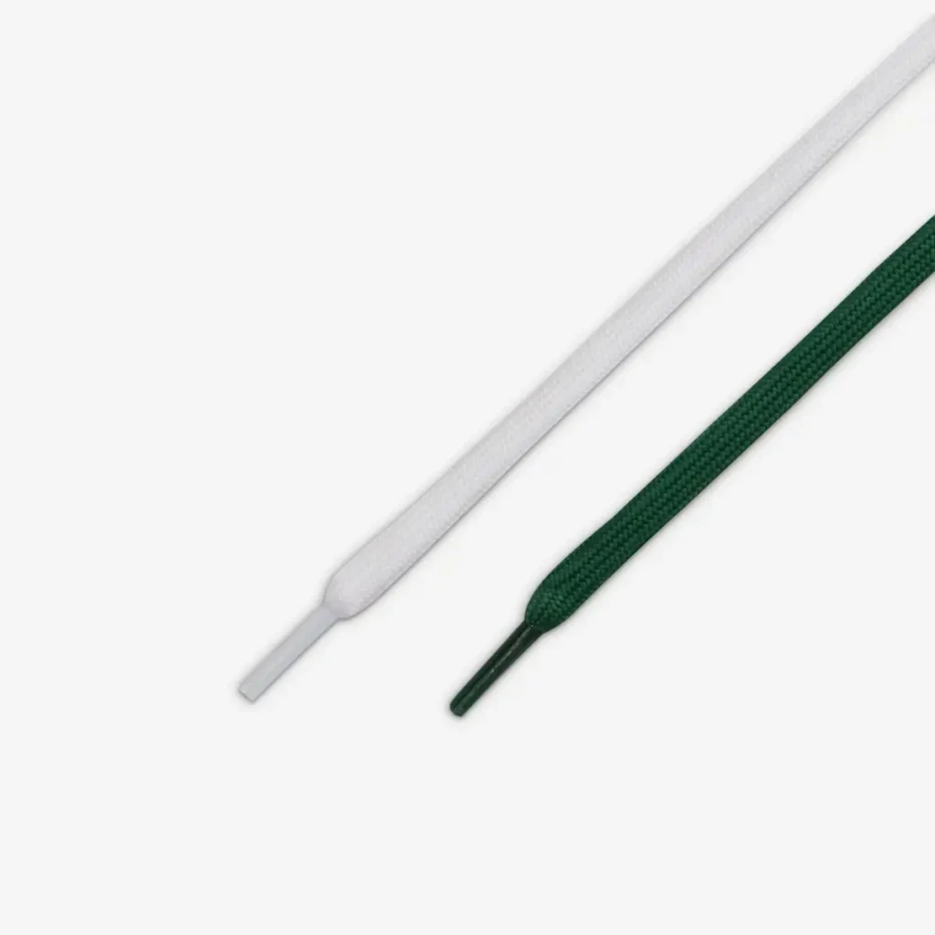 A close-up view of two shoelaces for the Nike LeBron 23 “From This Point Forward,” one in white and one in dark green, each with matching aglets, displayed on a clean white background