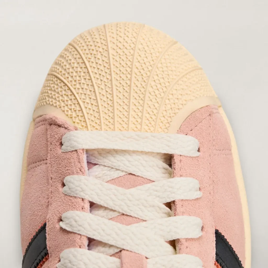 Close-up of the SpongeBob SquarePants x adidas Superstar “Patrick Star” showing the textured cream shell toe, pink suede upper, and thick white laces, captured from an overhead angle on a light background