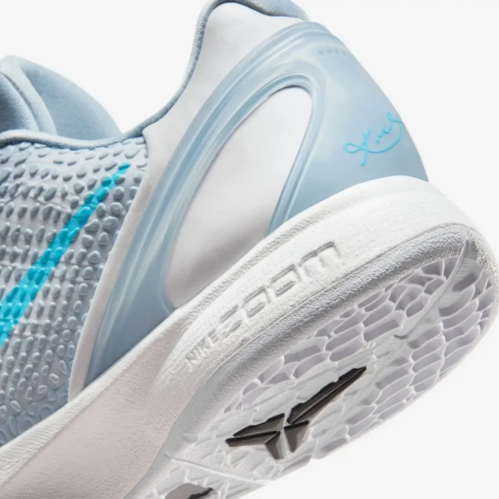 A close-up view of the Nike Kobe 6 Protro “Caitlin Clark” heel, highlighting the icy blue TPU heel counter with Caitlin Clark’s signature stamped in bright blue. The snakeskin-textured upper transitions into a white midsole embossed with “Nike Zoom,” while the translucent outsole shows the hexagonal traction pattern and Kobe’s sheath logo beneath