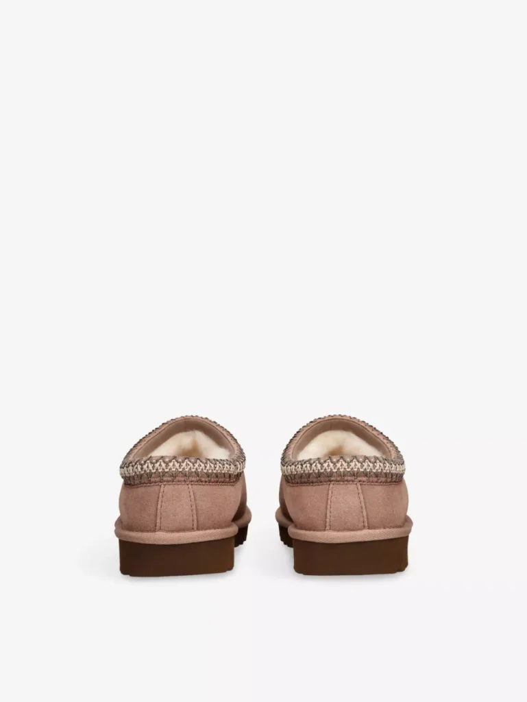 UGG Tasman II suede slippers shown from the rear, highlighting the low back profile, braided embroidered collar trim, suede heel construction, and thick dark rubber outsole on a clean white background