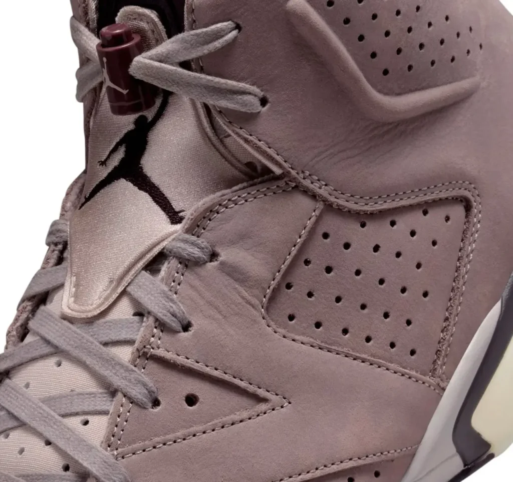 Close-up of the Air Jordan 6 × A Ma Maniére “Smokey Mauve,” showing the soft mauve suede upper, perforated side panel, satin tongue with embroidered Jumpman logo, and burgundy lace toggle, highlighting the shoe’s premium textures and craftsmanship