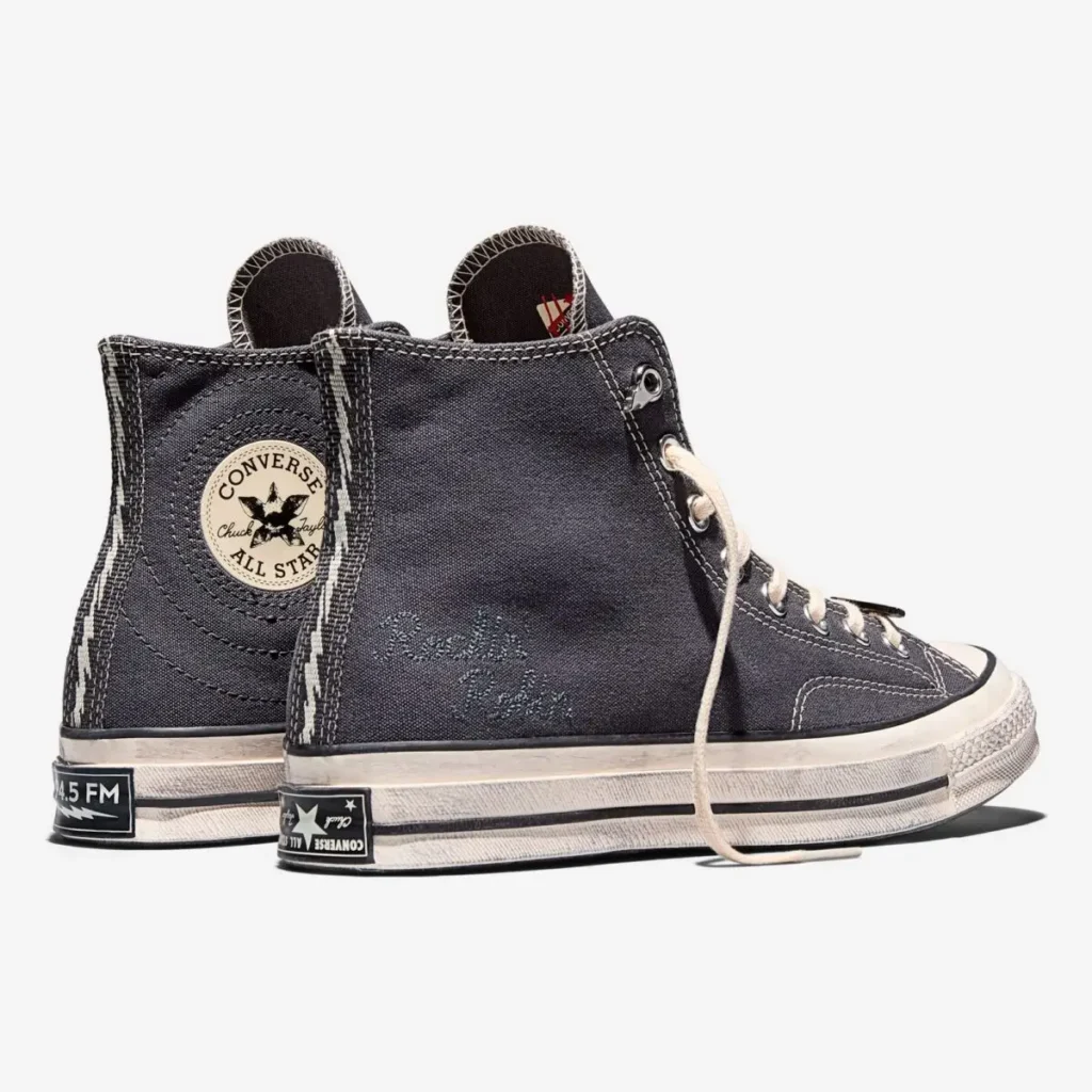 Rear and side view of the Stranger Things x Converse Chuck 70 “WSQK The Squawk” sneakers, showing the charcoal canvas upper, cream stitching, vintage-style off-white midsoles, and embroidered WSQK text on the heel panel. The classic Converse All Star patch appears on the inner ankle, with custom radio-frequency graphics printed on the heel badge against a clean white background