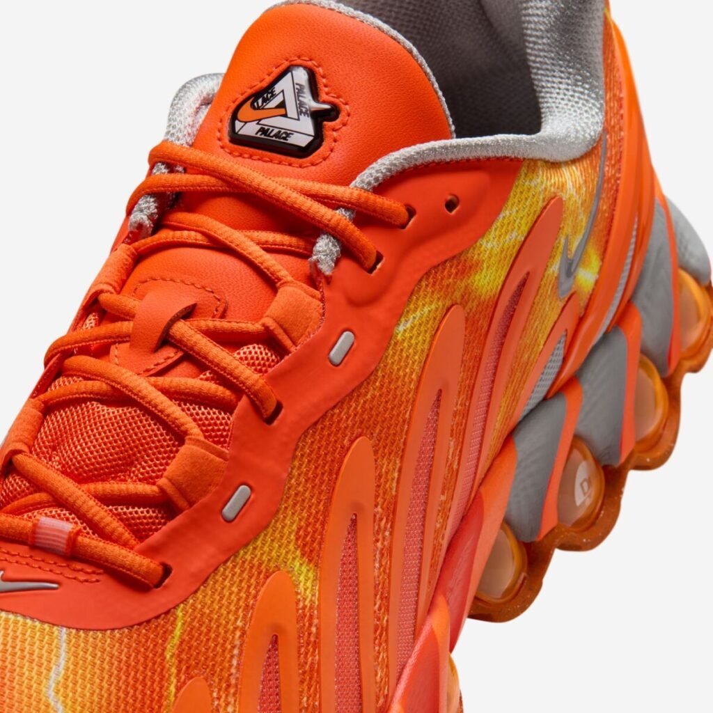 Close-up of the Palace x Nike Air Max DN8 “Safety Orange” showing the bright orange mesh and synthetic upper, tonal laces, metallic silver Swoosh, and co-branded Palace–Nike tongue badge above the sculpted DN8 Air sole