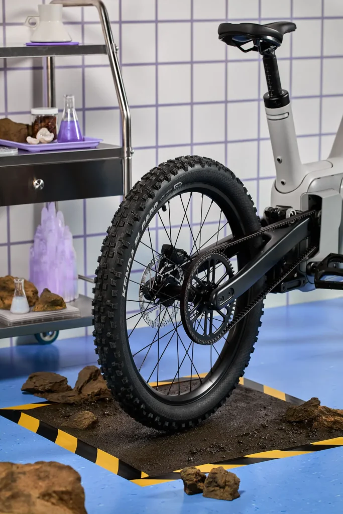 Rear view of the ALSO TM-B electric bike highlighting the belt-driven drivetrain, rear disc brake, and rugged all-terrain tire, staged on a test platform to emphasize durability, torque delivery, and EV-inspired engineering performance