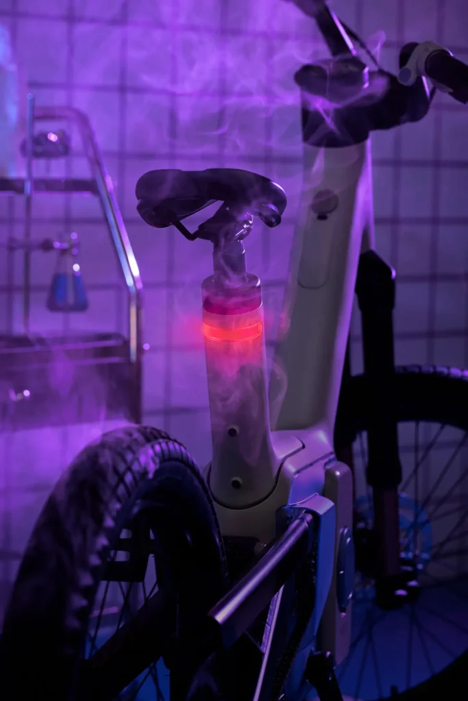 Rear section of the ALSO TM-B electric bike illuminated with purple lighting, highlighting the integrated rear light within the seatpost, sculpted frame lines, and belt-drive system, emphasizing safety-focused visibility and EV-inspired design aesthetics