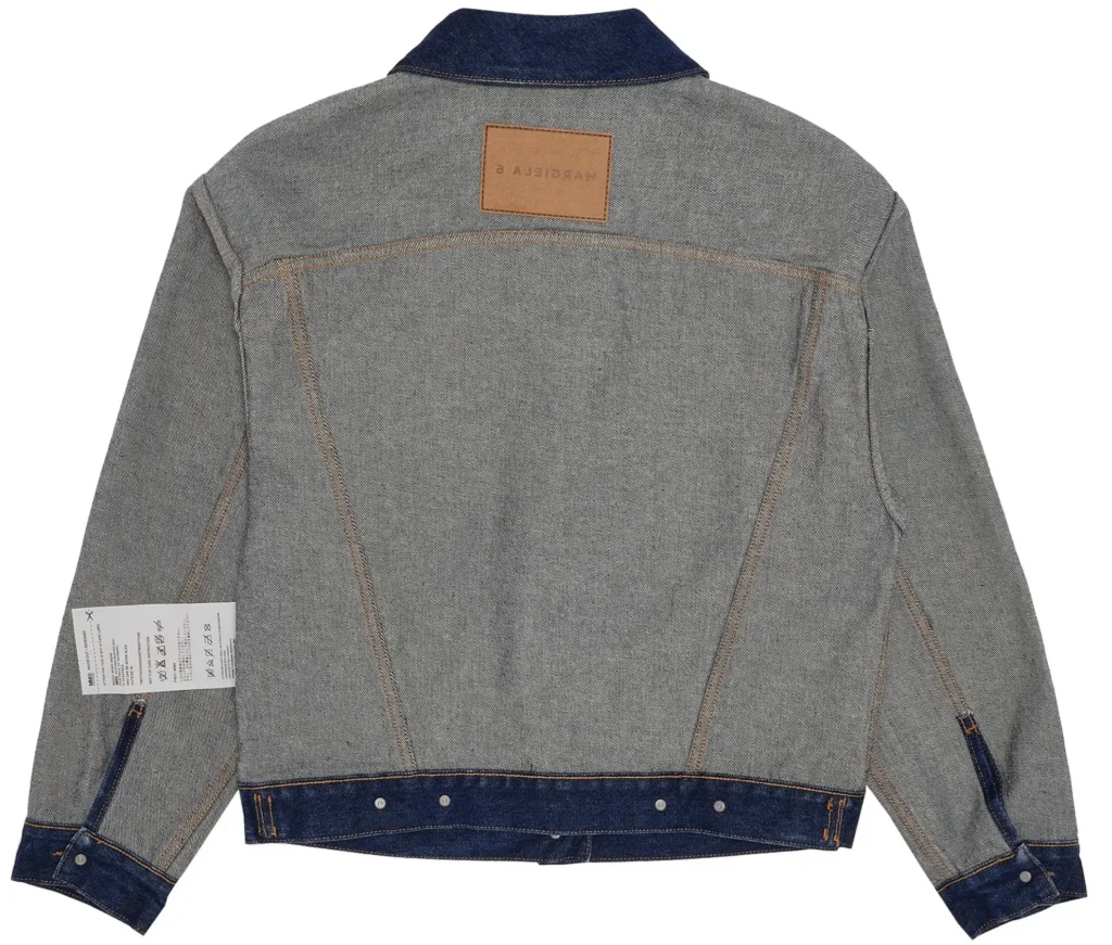 MM6 Maison Margiela Reversed Denim Jacket “Raw” back view laid flat on a white background, showcasing inside-out construction with exposed seam lines, grey-toned reversed denim panels, contrast tan stitching, darker indigo denim collar and hem band, adjustable button tabs at the waist, raw edge detailing, and a leather Maison Margiela label centered below the collar