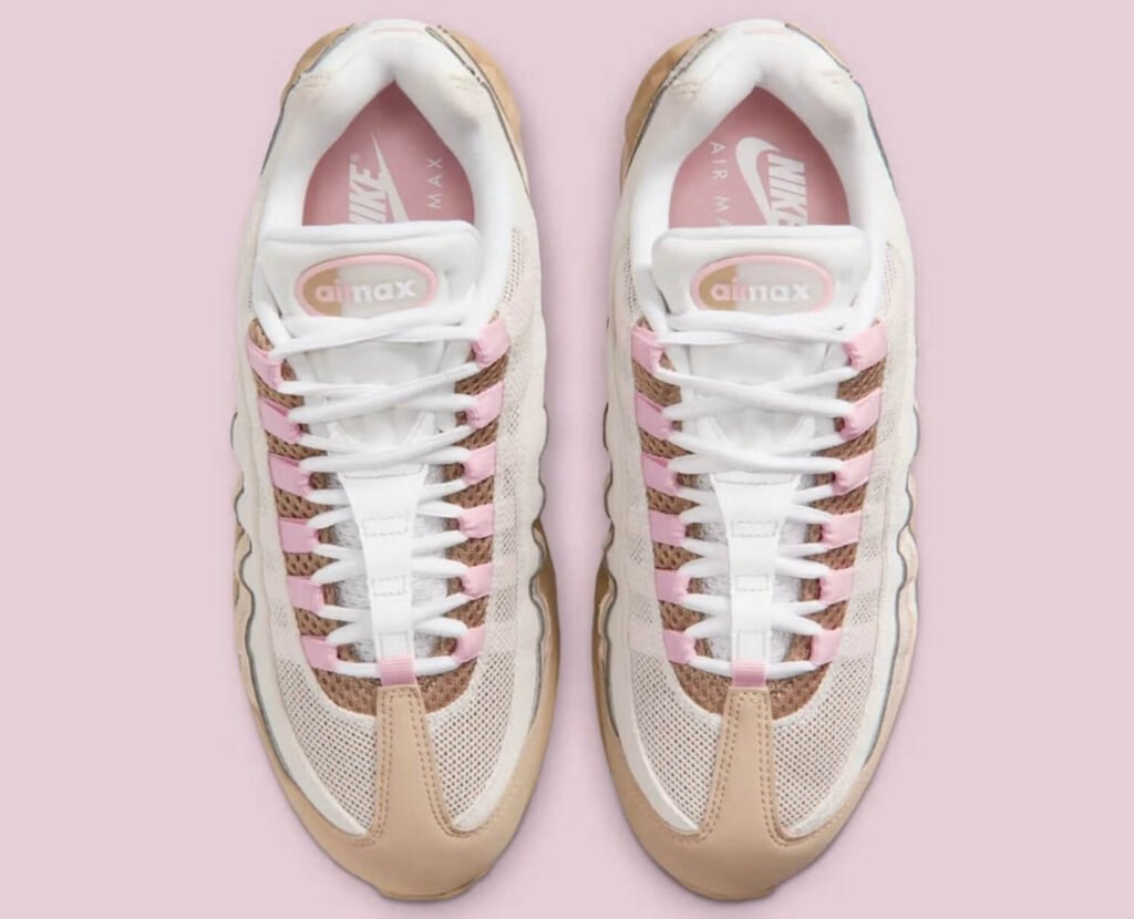 Top-down view of the Nike Air Max 95 “Linen,” showing white mesh uppers with beige suede overlays, soft pink lace loops, white laces, and pink Air Max branding on the tongue and insoles, set against a pale pink background