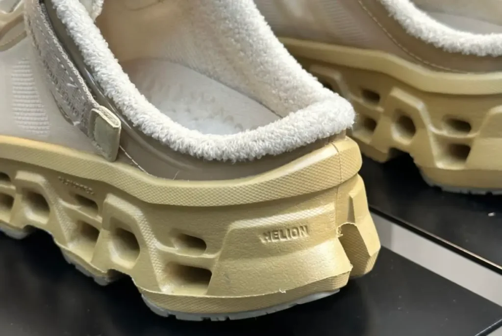 Close-up of the heel on beige On Share sneakers at Paris Fashion Week, showing the fleece-lined collar, translucent upper, strap hardware, and a chunky perforated midsole stamped with “HELION” cushioning technology