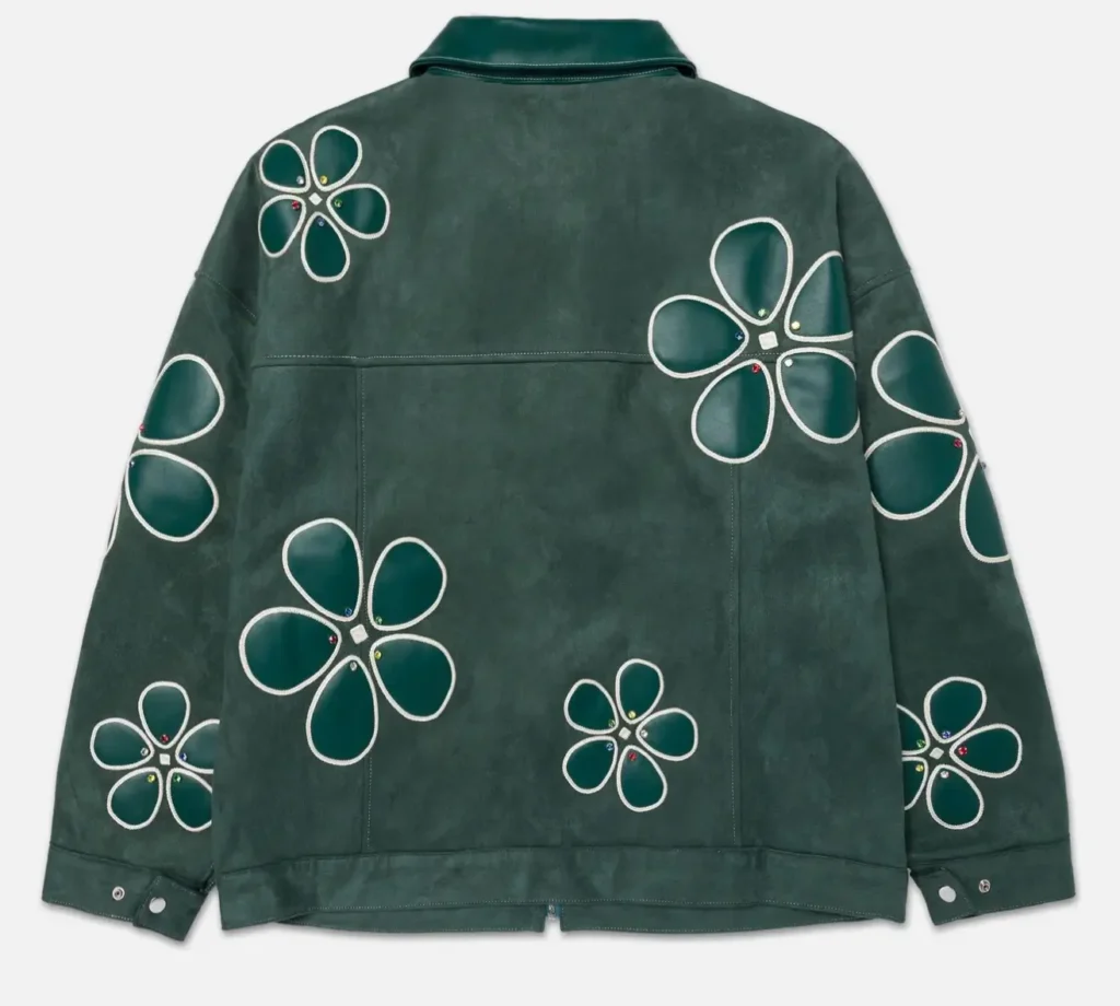Back view of a dark green suede work jacket covered with oversized floral appliqué motifs, featuring a leather collar, seam-panel construction, adjustable cuff snaps, and jewel-accented flower centers on a clean white background