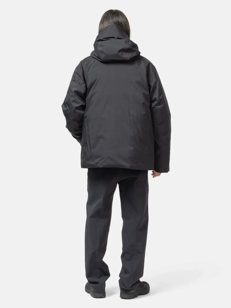 Rear view of a model wearing the VEILANCE Sorin Down Jacket in black, highlighting the clean back panel construction, sculpted hood shape, matte technical fabric, and relaxed, insulated fit designed for urban winter conditions