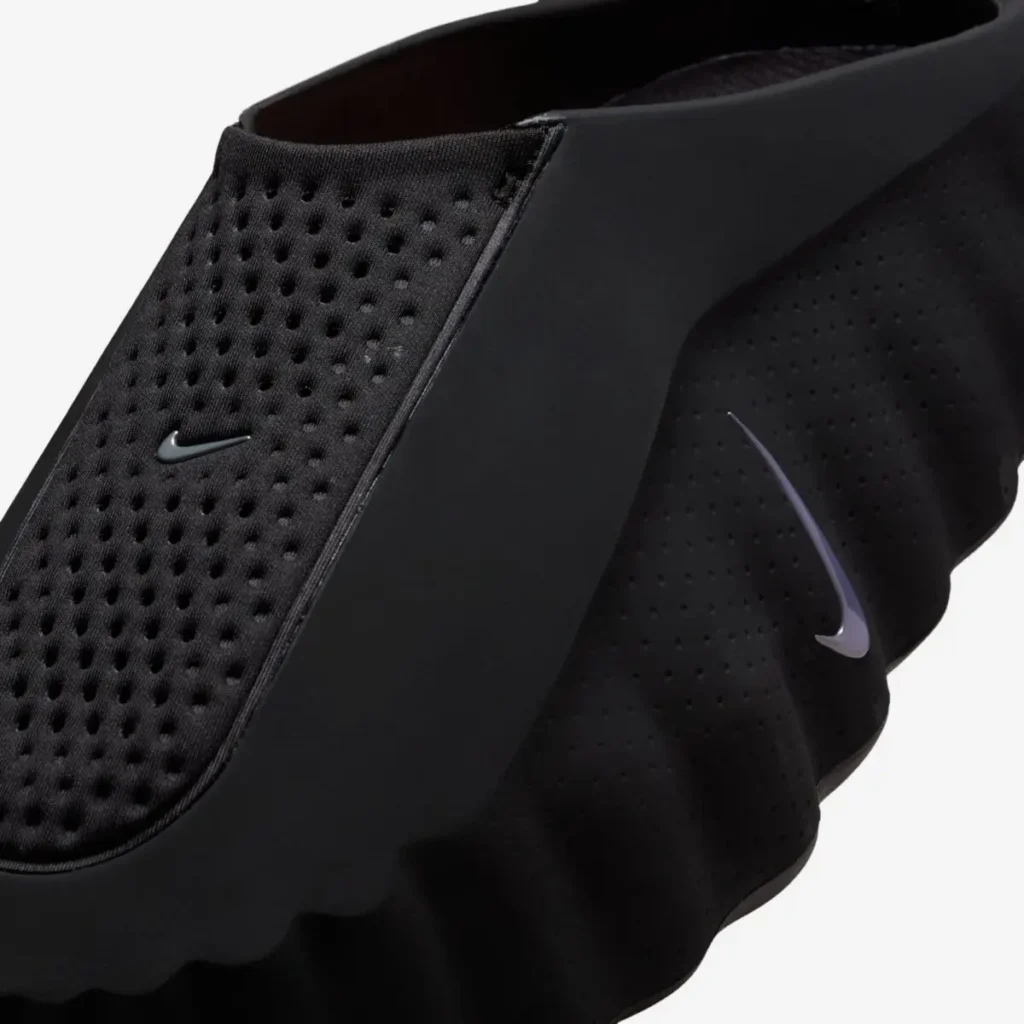 Close-up of the Nike Mind 001 “Black” sandal showing textured perforated upper, sculpted foam sidewall, and subtle Swoosh branding
