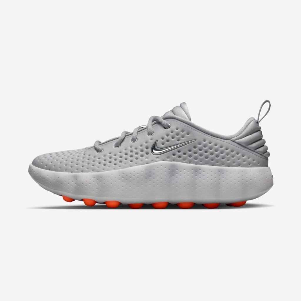 Side profile of the Nike Mind 002 “Light Smoke Grey” sneaker, highlighting the perforated grey upper, chrome Swoosh on the midfoot, thick sculpted foam midsole with subtle texture, heel pull tab, and the bright orange node-based outsole visible beneath