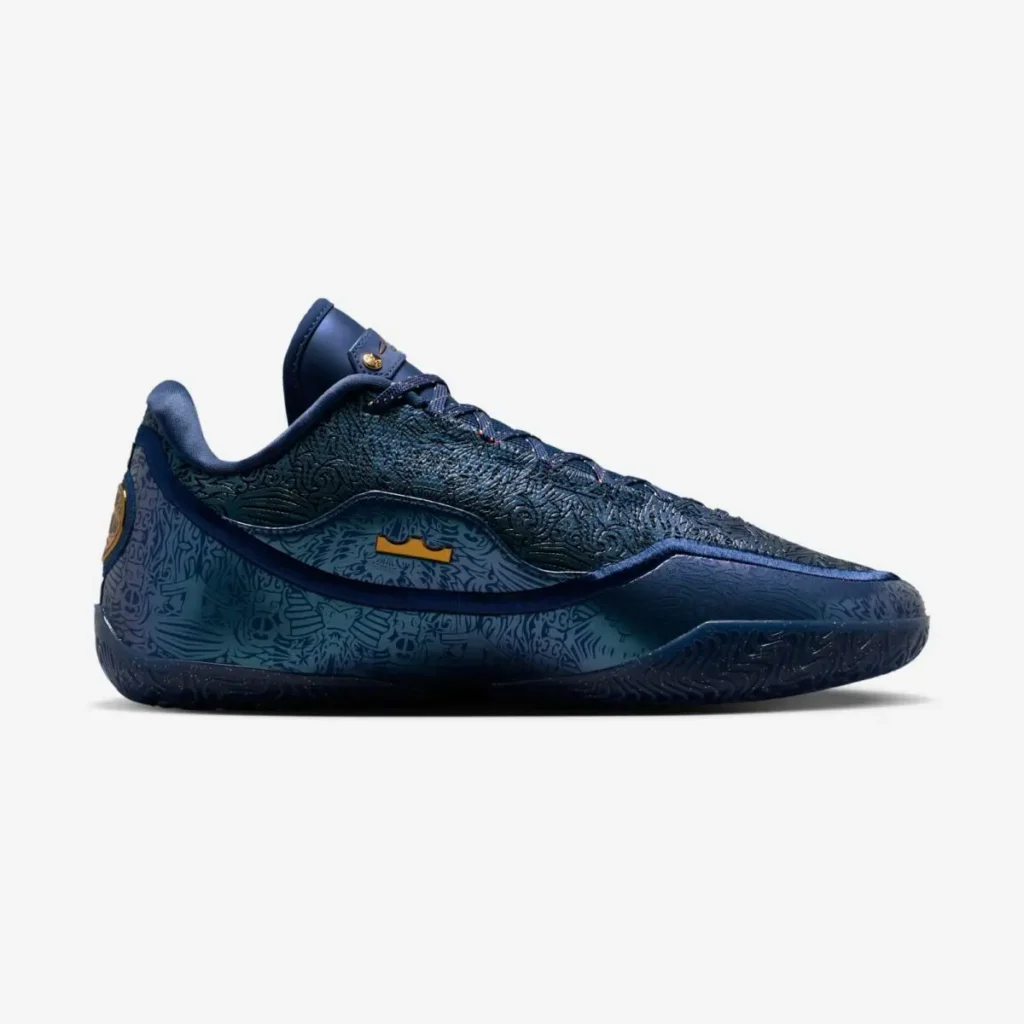Lateral side view of the Nike LeBron 23 “Out For Redemption” sneaker in dark navy with embossed abstract graphics along the upper and midsole, metallic gold LeBron emblem at the heel, gold accent panel near the midfoot, speckled black outsole, and padded low-cut collar on a white background