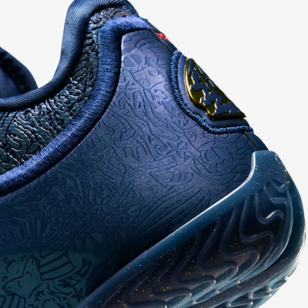 Close-up of the heel on the Nike LeBron 23 “Out For Redemption” shoe in dark navy, highlighting embossed graphic textures, metallic gold heel badge, padded collar lining, and speckled sculpted outsole edge against a white background