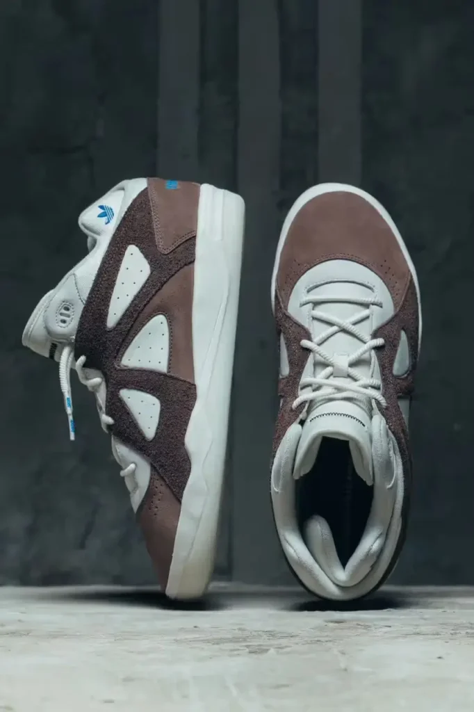 Brown suede and white leather BadBo 1.0 sneaker by Bad Bunny and adidas photographed floating against a dark concrete backdrop with blue Trefoil accents visible