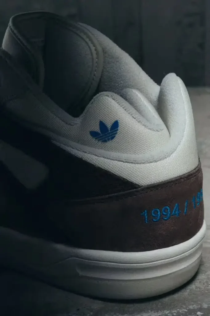 Close-up of the BadBo 1.0 heel by Bad Bunny and adidas showing blue Trefoil logo and embroidered “1994/1994” numbering on brown suede