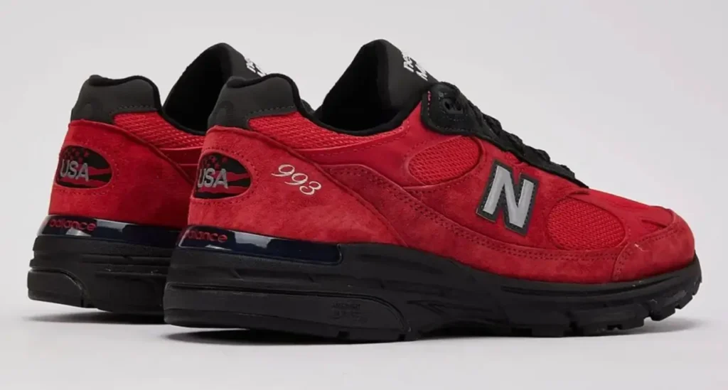 Rear three-quarter view of the New Balance Made in USA 993 “Red Suede” sneaker, showcasing vivid red suede panels, mesh underlays, black midsole and outsole, silver N logo, and “USA” heel branding against a clean studio background