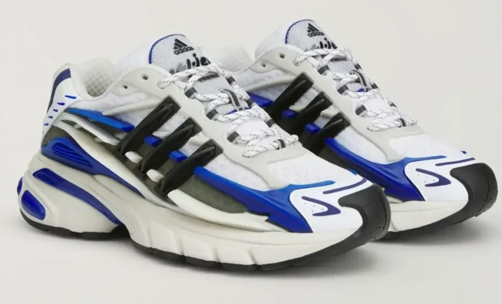 Pair of adidas Jellyfish ‘Royal’ sneakers shown in angled side view, featuring a futuristic chunky sole, white mesh upper, bold royal blue overlays, black sculpted cage detailing, and technical rope laces emphasizing the shoe’s fluid, modern running-inspired design