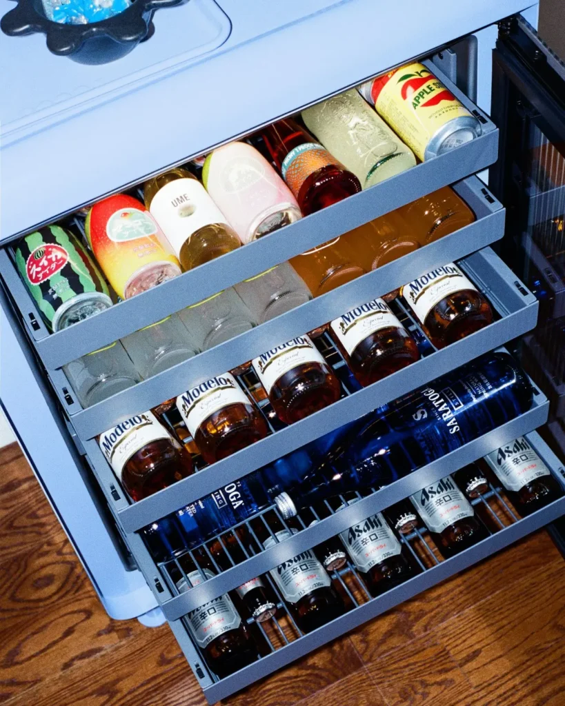 Rocco Ice Blue smart fridge with open pull-out shelves displaying neatly organized beverages, showcasing modular storage design, compact cooling efficiency, and modern lifestyle functionality